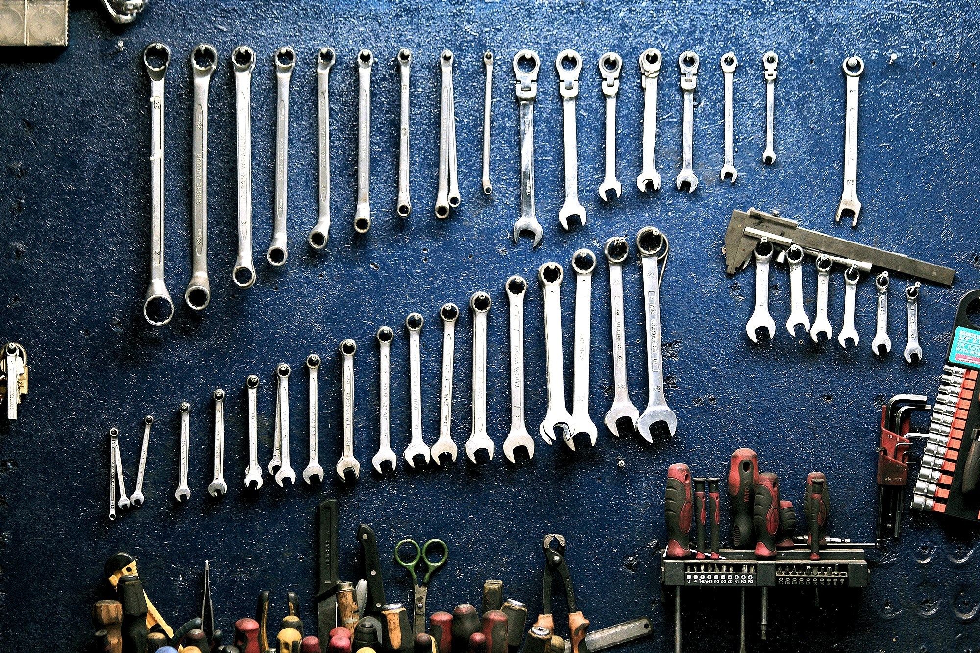 Multiple spanners of various sizes hanging on a blue-colored wall