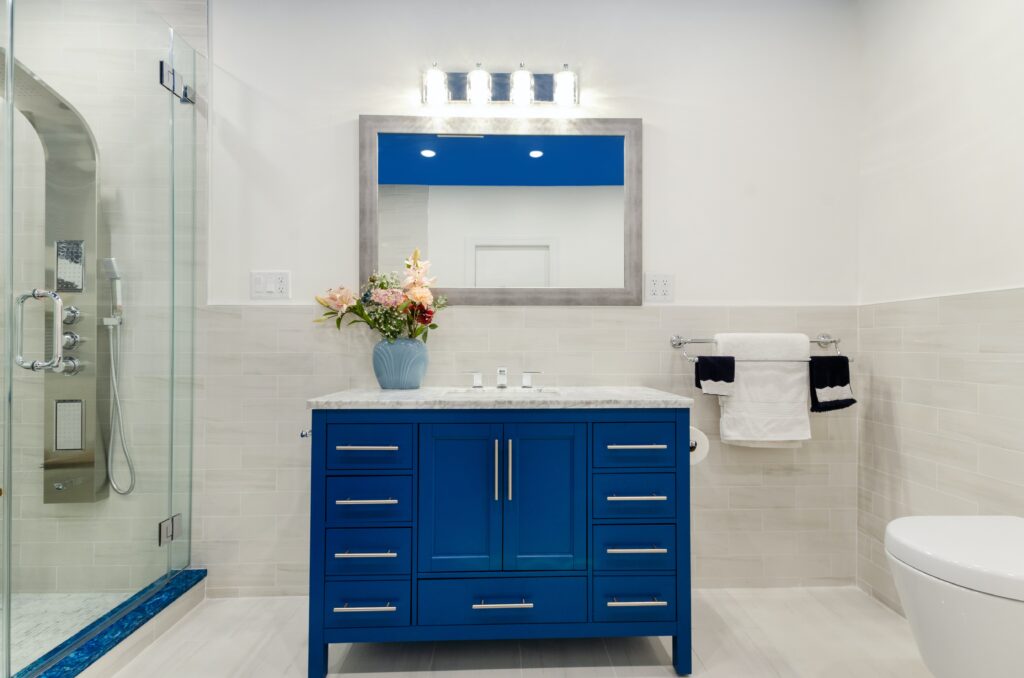 A white bathroom with matching blue accents in the ceiling, small tiles in front of the shower, and under-sink cabinets.