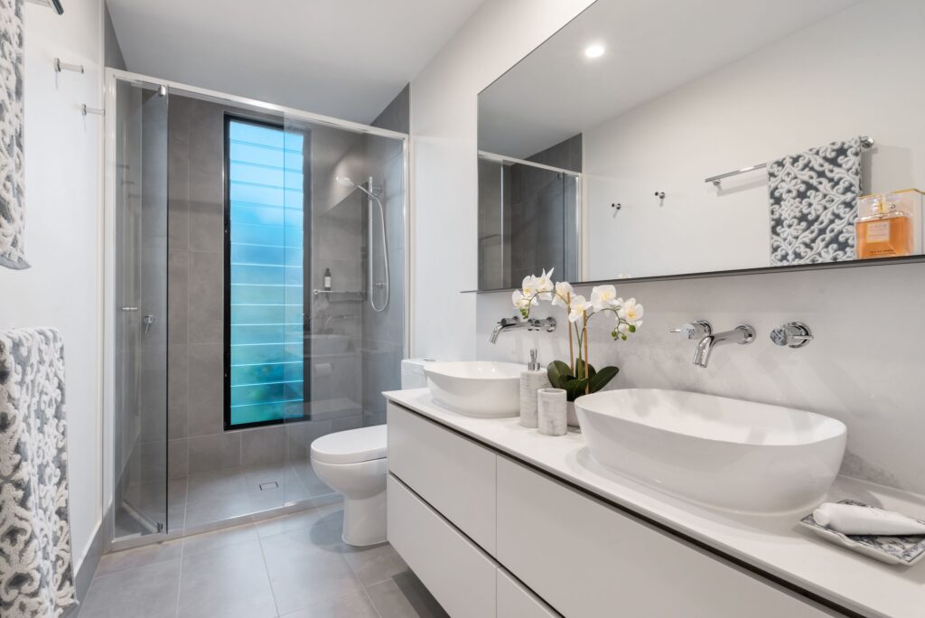 A beautiful white bathroom with white flowers placed between the two wash basins.